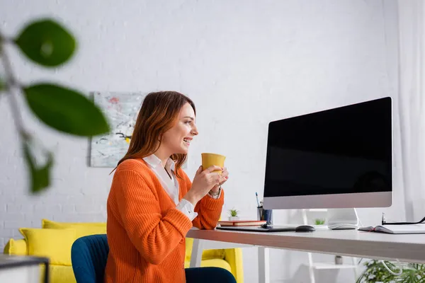 Zadowolona Kobieta Filiżanką Herbaty Patrząc Monitor Komputera Pustym Ekranem Domu — Zdjęcie stockowe