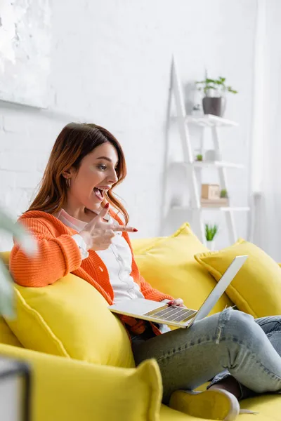 Amazed Freelancer Pointing Laptop While Sitting Yellow Couch Blurred Foreground — Stock Photo, Image