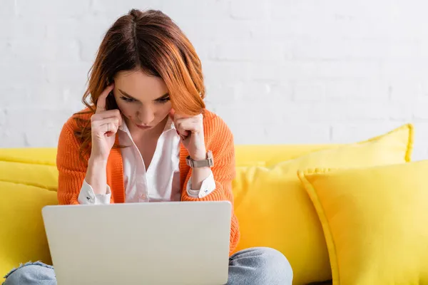 Pensive Freelancer Menyentuh Kepala Ketika Duduk Sofa Kuning Dengan Laptop — Stok Foto