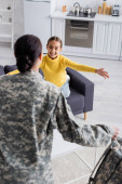 Preteen Kind lächelt verschwommene Mutter in Militäruniform zu Hause an 
