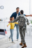 Glücklicher Mann und Kind stehen neben Mutter in Militäruniform und amerikanischer Flagge zu Hause 
