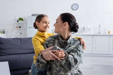 Gülümseyen çocuk evde askeri üniformalı annesine sarılıyor. 