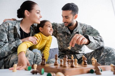 Askeri üniformalı mutlu bir adam satranç figürünü evinde kız ve eşinin yanında tutuyor. 