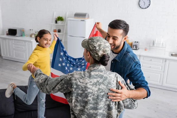 Família Positiva Com Bandeira Americana Abraçando Mulher Uniforme Militar Cozinha — Fotografia de Stock