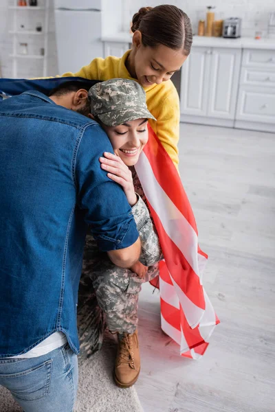 在家里 穿着军服的男人拥抱着妻子 女儿身边挂着美国国旗 — 图库照片