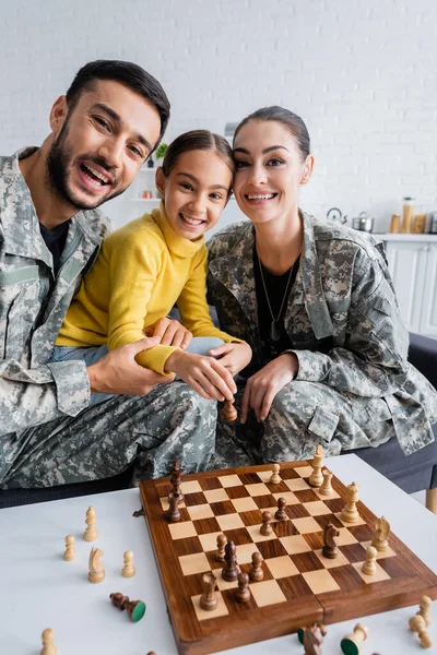 Leende Föräldrar Militäruniform Tittar Kameran Nära Barn Med Schackfigur Soffan — Stockfoto