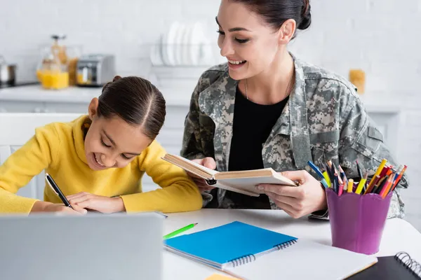 Sonriente Madre Uniforme Militar Sosteniendo Libro Cerca Hija Con Pluma — Foto de Stock