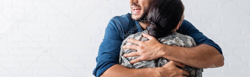 Cropped view of cheerful man embracing wife in military uniform at home, banner 