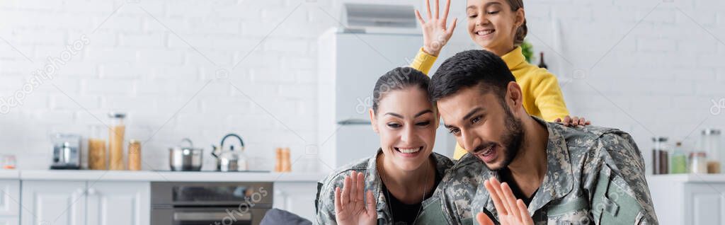 Smiling parents in military uniform waving hands near preteen child at home, banner
