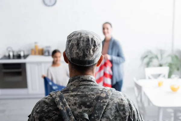 Soldat Kamouflage Står Nära Suddig Familj Med Amerikansk Flagga Hemma — Stockfoto