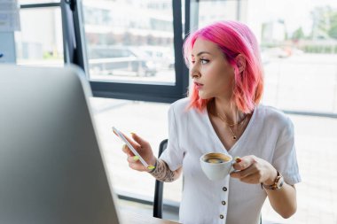 Pembe saçlı, elinde kahve fincanı ve akıllı telefonu olan genç bir menajer.