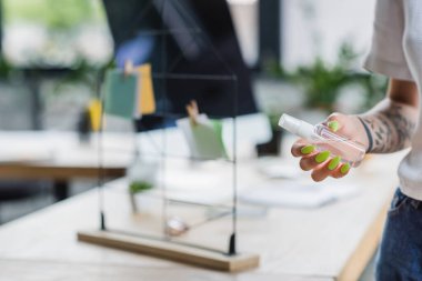 Ofiste dezenfektanla şişe tutan dövmeli bir iş kadını görüntüsü.
