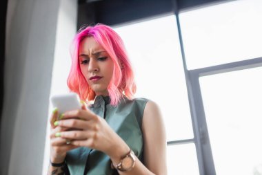Akıllı telefon kullanan pembe saçlı iş kadınının düşük açılı görüntüsü
