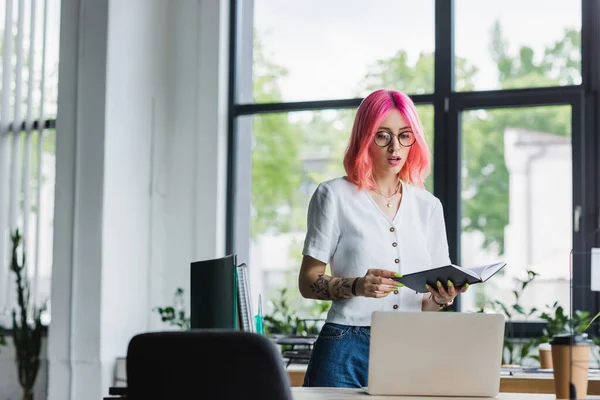 Młoda Bizneswoman Różowymi Włosami Trzymając Notatnik Patrząc Laptopa — Zdjęcie stockowe