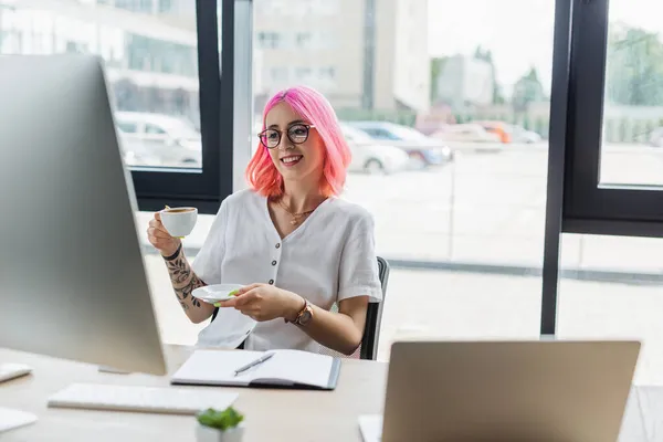 Szczęśliwy Businesswoman Różowymi Włosami Trzymając Filiżankę Kawy Patrząc Monitor Komputera — Zdjęcie stockowe