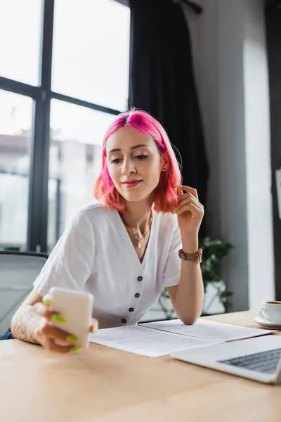 Χαμογελαστή Επιχειρηματίας Ροζ Μαλλιά Κοιτάζοντας Smartphone Κοντά Στο Laptop — Φωτογραφία Αρχείου