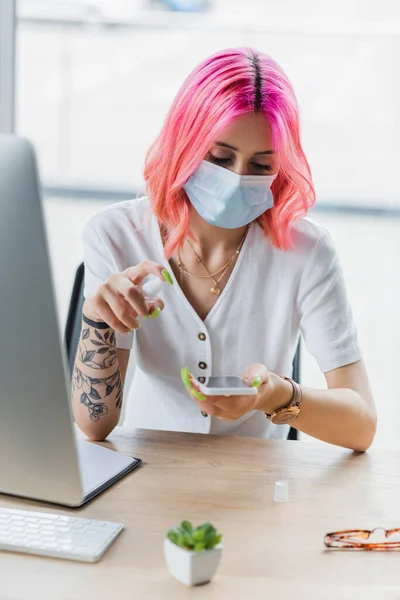 医療用マスクの若い実業家がオフィスでスマートフォンにサニタイザーを吹きかけ — ストック写真