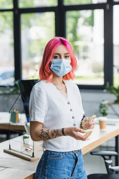 ピンクの髪をした入れ墨のビジネスマン女性オフィスで手に消毒剤を噴霧 — ストック写真