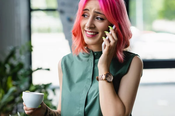 ピンク色の髪の明るい女性とオフィスでスマートフォンで話している間にコーヒーを飲みながらピアス — ストック写真