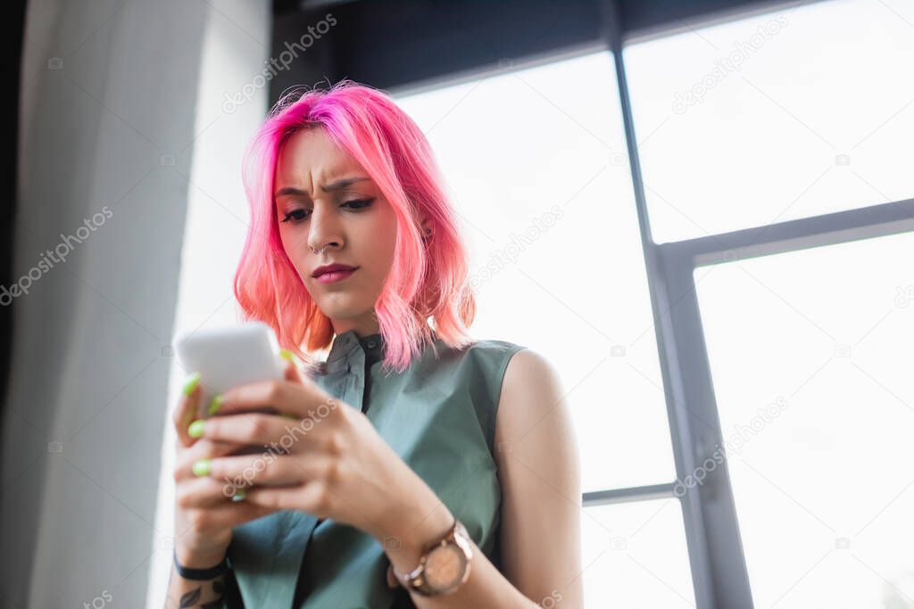 low angle view of focused businesswoman with pink hair using smartphone