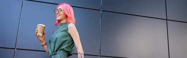 happy and tattooed businesswoman with pink hair holding paper cup outside, banner