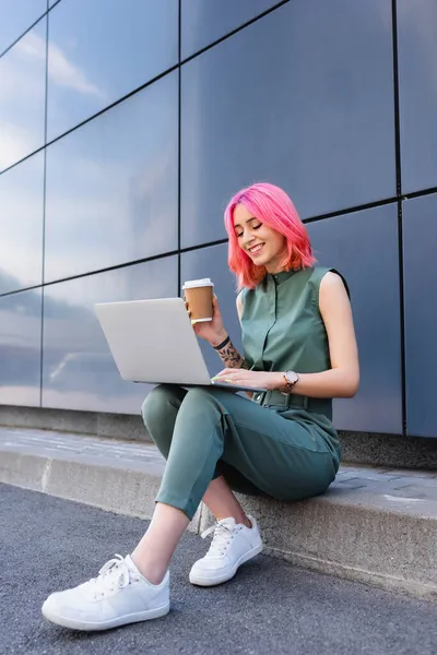 Positive Businesswoman Pink Hair Holding Paper Cup Using Laptop — Stock Photo, Image