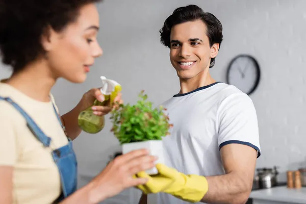 Happy Young Man Holding Plant Blurred African American Woman Spray — Stock Photo, Image