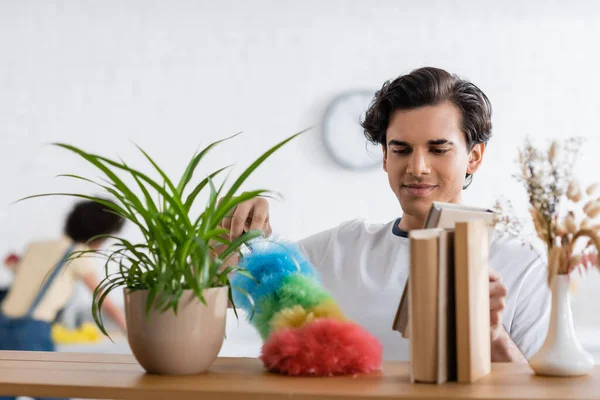 Young Man Cleaning Wooden Shelf Dust Brush Plants Books — Stock Photo, Image