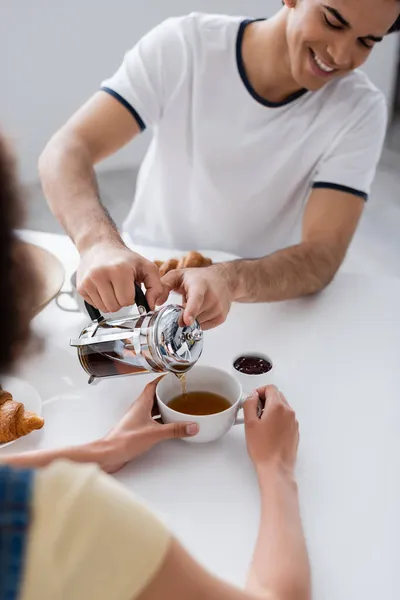 Happy Man Pouring Tea Cup Blurred African American Girlfriend — Stock Photo, Image