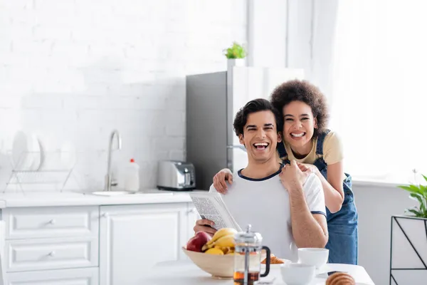 Happy African American Woman Hugging Boyfriend Newspaper Kitchen — Stock Photo, Image