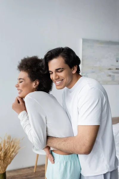 Cheerful Multiethnic Couple Laughing Hugging Bedroom — Stock Photo, Image