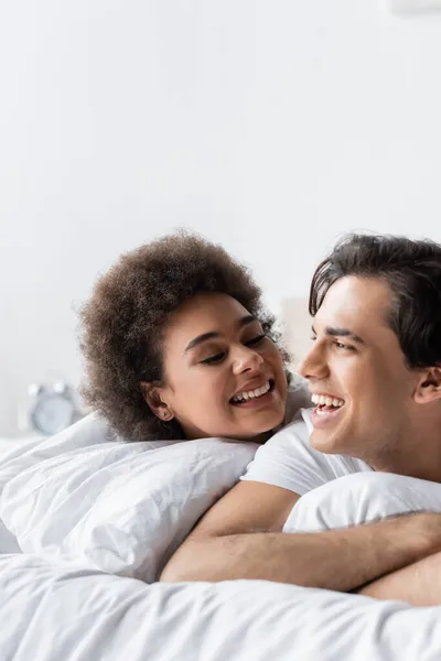 Fröhliches Interrassisches Paar Lächelt Während Auf Dem Bett Liegt — Stockfoto