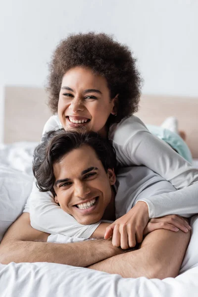 Alegre Interracial Casal Sorrindo Enquanto Abraçando Cama — Fotografia de Stock