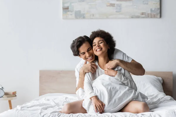 Positivo Interracial Casal Sorrindo Enquanto Abraçando Cama — Fotografia de Stock