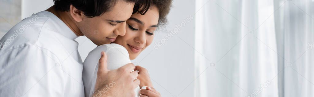 young man hugging smiling african american girlfriend at home, banner