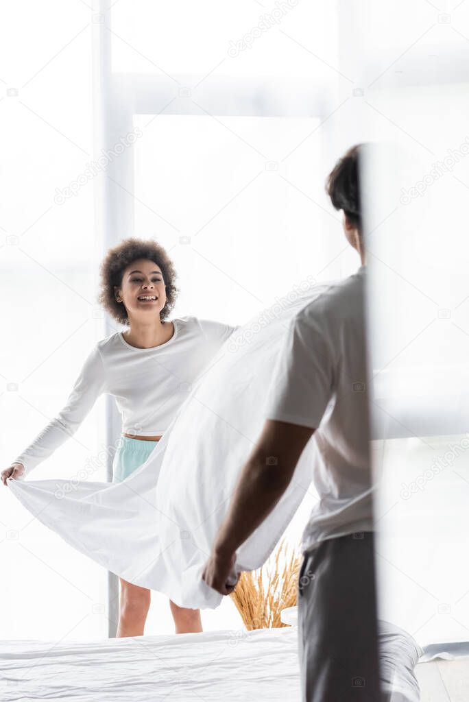 cheerful african american woman arranging bed sheet with boyfriend 