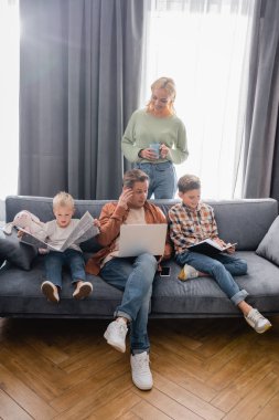 Çocuklar dizüstü bilgisayarı ve gazetesi olan çocuklar kanepede oturuyorlar.