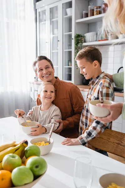 Criança Alegre Comendo Flocos Milho Perto Pais Irmão Cozinha — Fotografia de Stock