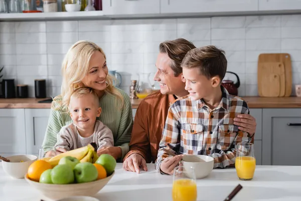 Lyckliga Par Omfamnar Barn Frukost Nära Färska Frukter Och Apelsinjuice — Stockfoto