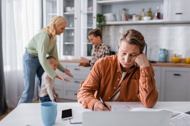 Bulanık arka planda aile oyunu oynarken mutfakta çalışan yorgun adam.