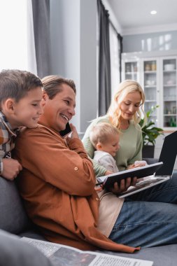 Oturma odasındaki kanepe ailesinin yanında akıllı telefondan konuşan neşeli adam.