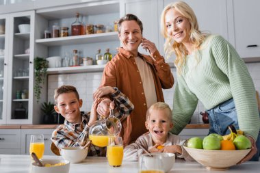 Akıllı telefondan konuşan ve ailemle kahvaltı ederken portakal suyu döken bir adam.