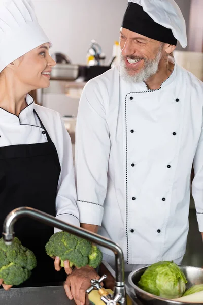 Chefs Positivos Sosteniendo Verduras Cerca Del Grifo Cocina Del Restaurante — Foto de Stock