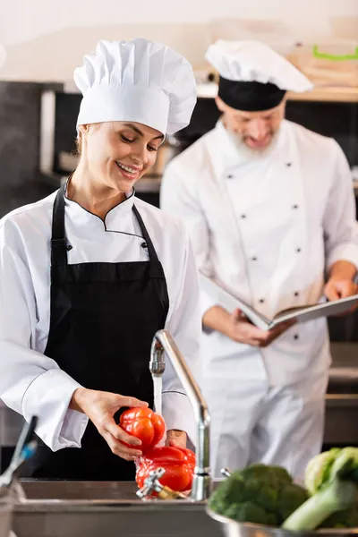 Chef Sonriente Lavando Verduras Cerca Colega Con Libro Cocina Cocina —  Fotos de Stock