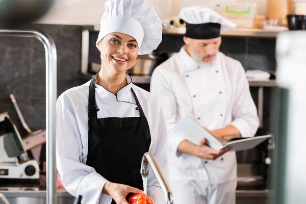 Chef Sorrindo Olhando Para Câmera Enquanto Lava Pimentão Perto Colega — Fotografia de Stock