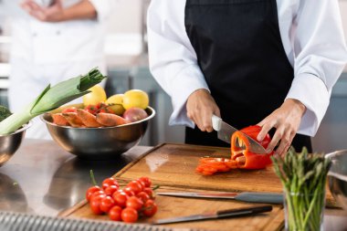 Mutfakta bıçakların ve sebzelerin yanında dolma biber kesen şefin kırpılmış görüntüsü. 