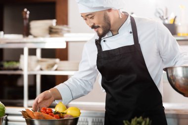 Asyalı şef restoran mutfağında taze sebzelere bakıyor. 