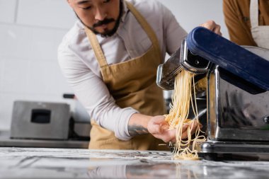 Mutfaktaki makarna makinesinde spagetti yapan bulanık Asyalı şefin görüntüsü. 