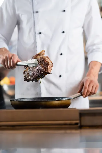 Vista Cortada Chef Segurando Carne Assada Pinças Perto Frigideira — Fotografia de Stock