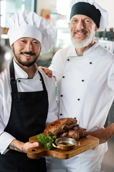 Chefs Multiétnicos Positivos Sosteniendo Carne Cocida Tabla Cortar Cocina — Foto de Stock